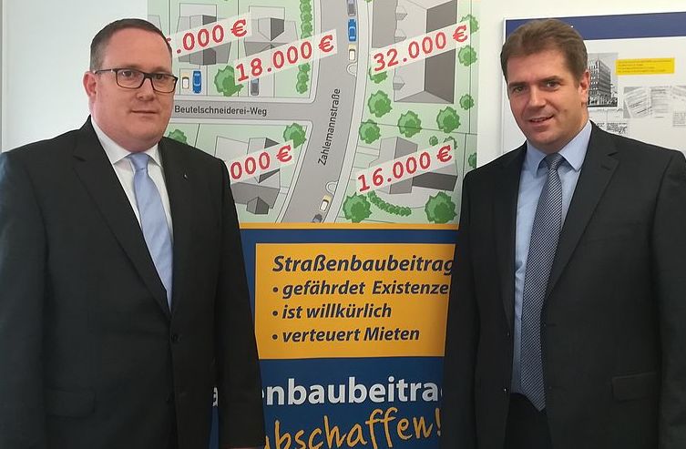 Markus Berkenkopf und Rik Steinheuer vor dem Plakat der Volksinitiative: Straßenbaubeitrag abschaffen!