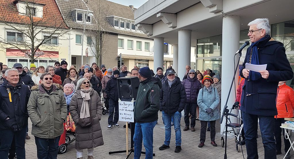 BdSt-Referent Jens Ammann (r.) auf der Demonstration in Mülheim a.d.R. am 15. Februar 2025. Er spricht auf dem Marktplatz zu einer Gruppe vor ihm stehender Menschen. Auf einem ihrer Plakate steht: "Wir Bürger sind nicht dumm, wir können rechnen"