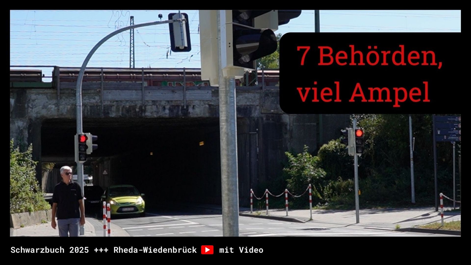 Zwei rote Ampeln und ein Fußgänger an einer Straße vor einer Bahnunterführung