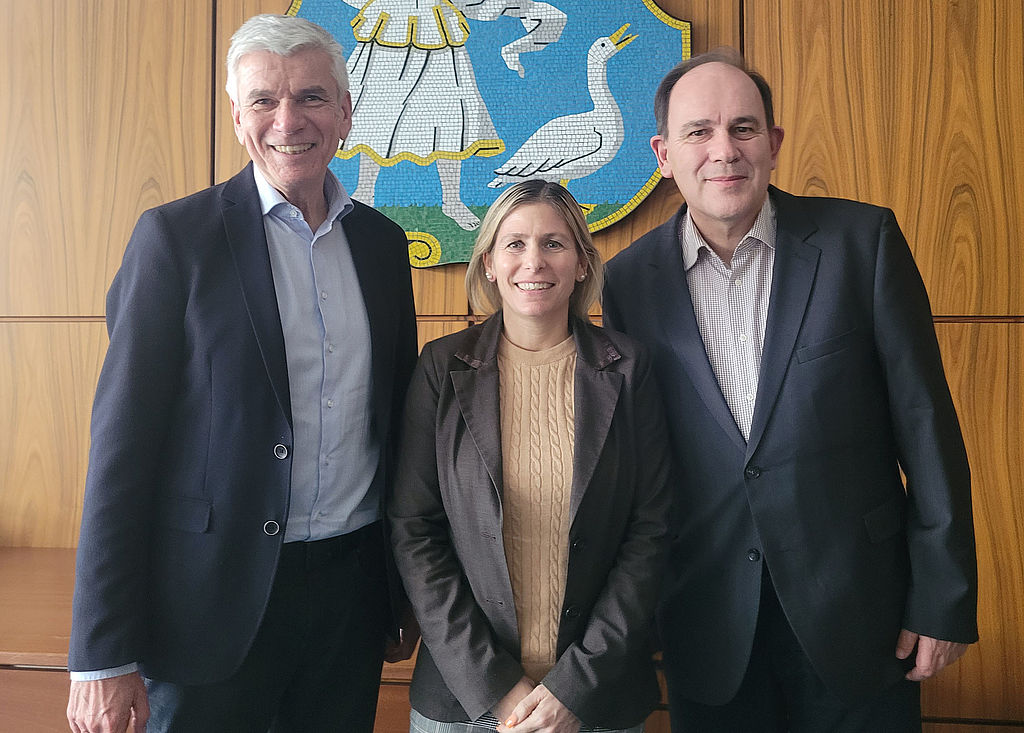 Drei nebeneinander stehende Personen unter dem Wappen von Monheim