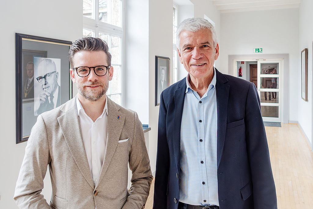 Mönchengladbachs Oberbürgermeister Felix Heinrichs (links) berichtete BdSt-Projektleiter Jens Ammann vom Rathaus der Zukunft. Zwei Männer im Gesprächsflur eines Rathauses, im Hintergrund Porträts ehemaliger Amtsinhaber an weißen Wänden